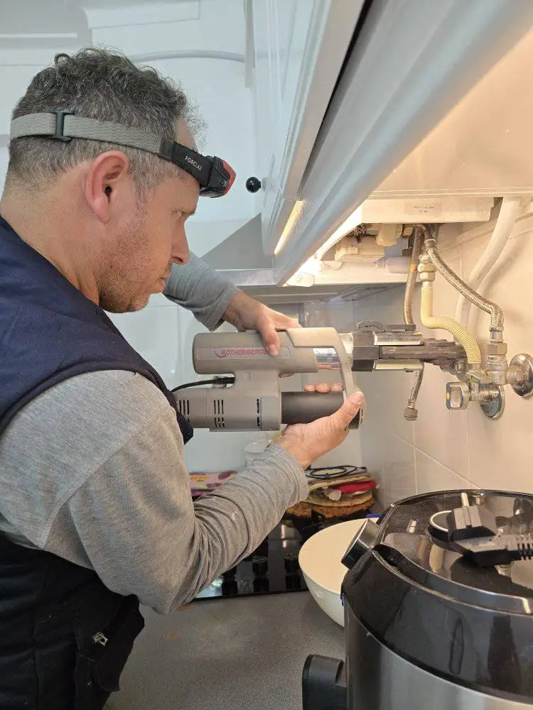 Técnico a limpar e desobstruir canalização o esquentador acima de um lava-loiça em Sintra.