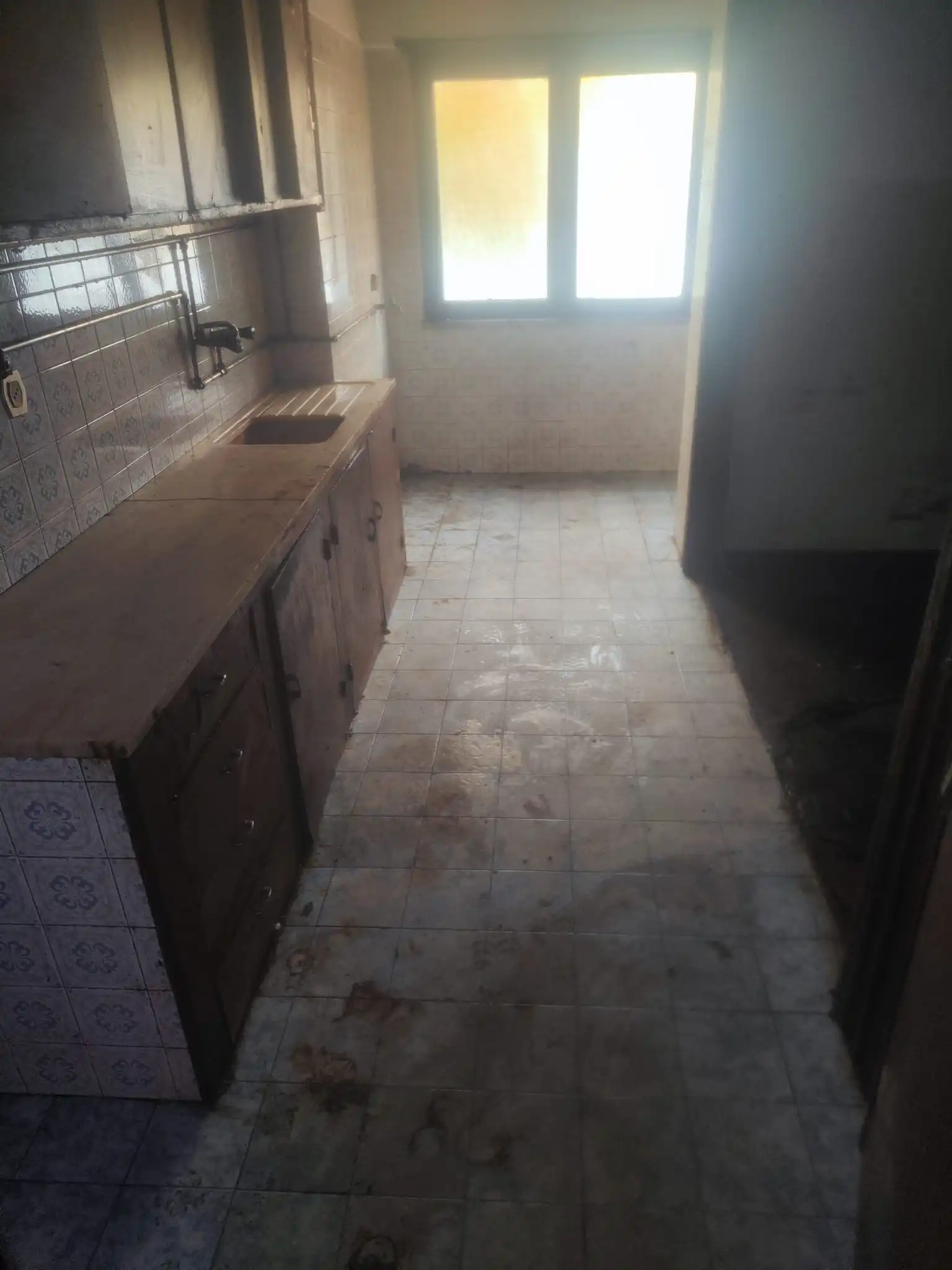 Mesma cozinha completamente transformada: bancadas brancas a brilhar sem qualquer resíduo, fogão com superfície polida e queimadores visíveis, lava-louças vazio e reluzente, chão lavado com acabamento uniforme e cantos livres de detritos.