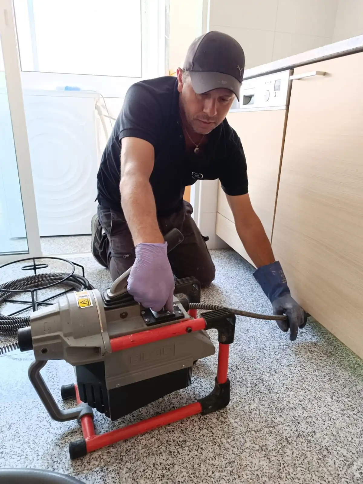 Profissional a operar máquina de desentupimento no interior de uma cozinha em Sintra.